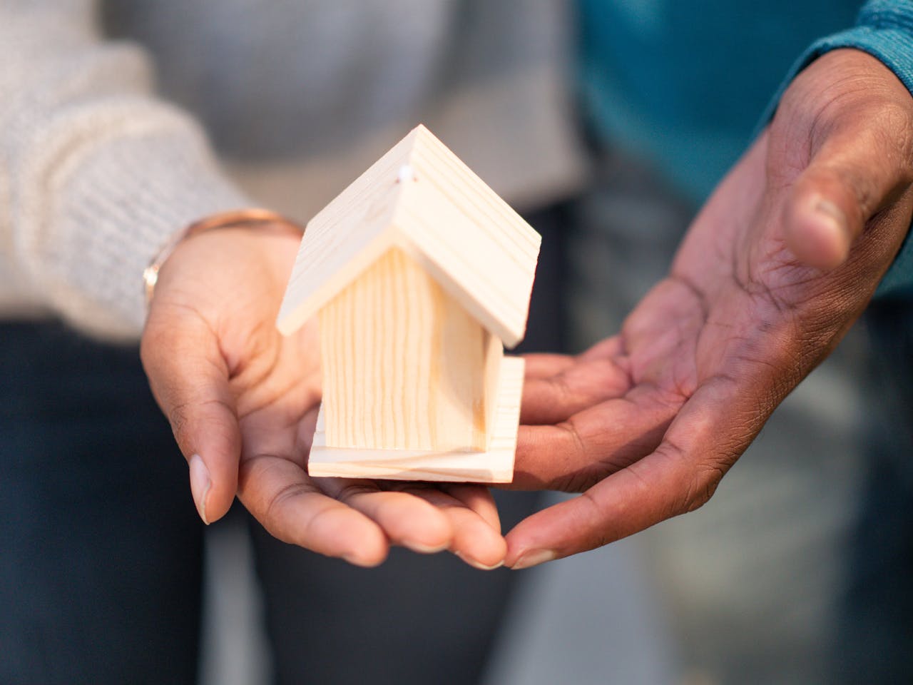 Close-up of hands holding a small wooden house, representing real estate and new home ownership.